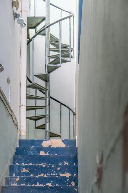 A narrow, worn staircase with blue-painted wooden steps, some of which have chipped paint revealing the wood beneath, leading to an upper floor in a residential property. Adjacent to the staircase on